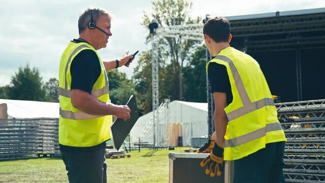 Male Production Team Moving Flight Case And Setting Up Outdoor Stage For Music Festival 