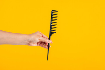 Black hair comb in hand isolated on yellow background