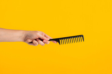 Black hair comb in hand isolated on yellow background - obrazy, fototapety, plakaty