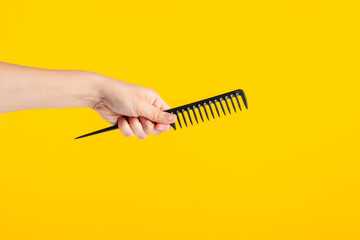 Black hair comb in hand isolated on yellow background