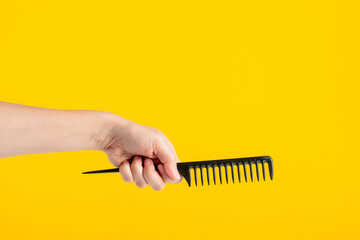 Black hair comb in hand isolated on yellow background