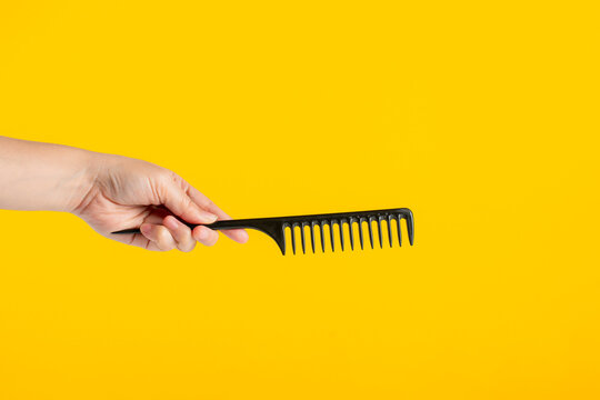 Black hair comb in hand isolated on yellow background