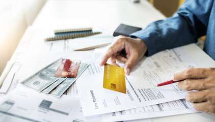 Asian businessman holding credit card to checking invoice and bank statement from online order, A...