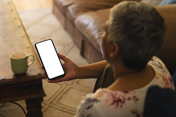 A mature biracial woman checks her phone at home, with copy space unaltered - Powered by Adobe