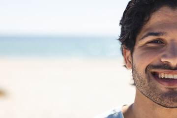 Young biracial man smiles brightly at the beach, with copy space