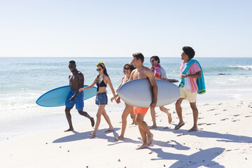 Diverse group of friends carry surfboards on a sunny beach