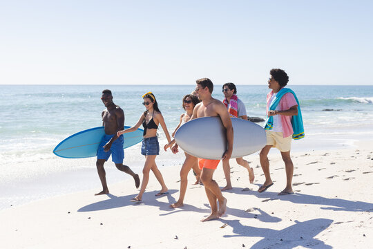 Diverse group of friends carry surfboards on a sunny beach - Powered by Adobe