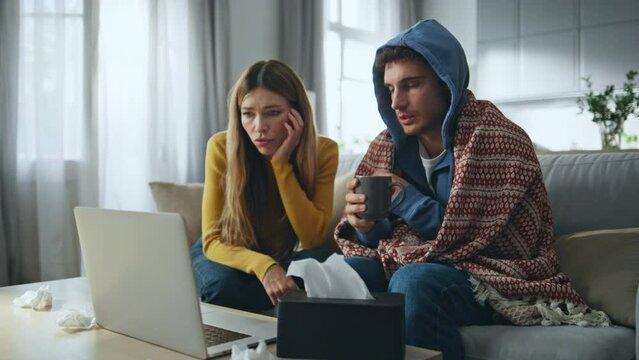 Sick couple calling doctor using laptop home. Wife measuring husband temperature