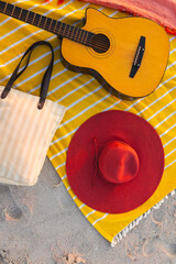 A beach setup features a guitar and a red hat on a yellow blanket