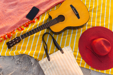 Fototapeta premium A guitar, hat, and smartphone rest on a beach blanket, with copy space