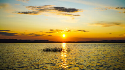 Obraz premium Golden sunset on the lake. Panoramic view of the lake and mountains. Light waves at golden hour. 