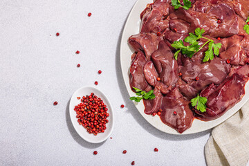 Raw chicken liver on stone background. Fresh ingredients ready for cooking, parsley, red pepper