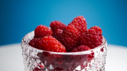 Raspberries in a crystal vase. Summer fresh raspberry berry on a blue background.
