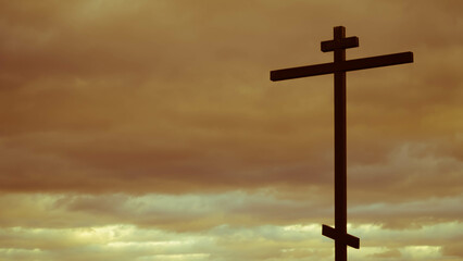 The holy Christian cross against the background of gloomy clouds in the sky. The concept of the resurrection of Jesus Christ. Easter background.
