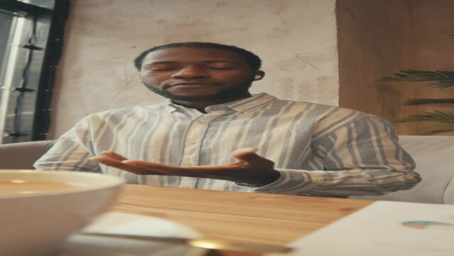 Vertical POV UGC of African American man putting in-ears and starting talking to camera while recording video for vlog in cafe