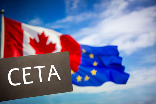 Schild mit der Aufschrift CETA vor den Flaggen von Kanada und der Europ&auml;ischen Union. Die Abk&uuml;rzung CETA steht f&uuml;r ein Freihandelsabkommen zwischen den beiden Partnern