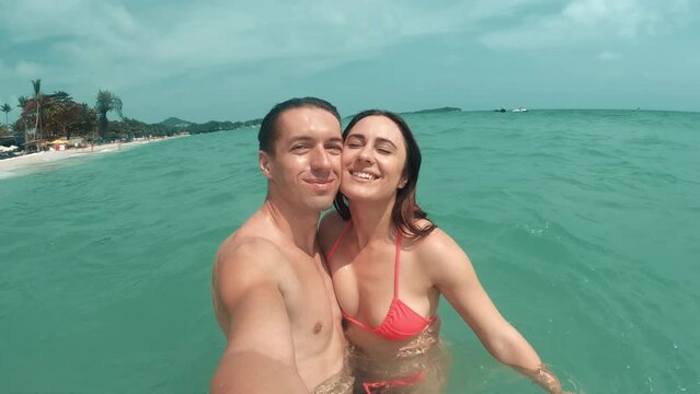 Selfie of loving couple in azure turquoise sea under bright sun. Happy couple enjoying romantic holiday at resort on hot summer day. Happy faces and closeness to each other show love couple.