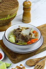 Sop daging sapi or Indonesian beef soup, served on ceramic white bowl with sambal and slices of lime. Selective focus with white marble background. 