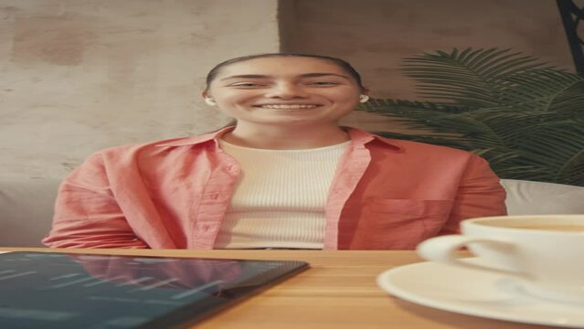 Vertical POV UGC of cheerful Caucasian lady speaking on video call or webinar about business graphics and charts while sitting in cozy cafe
