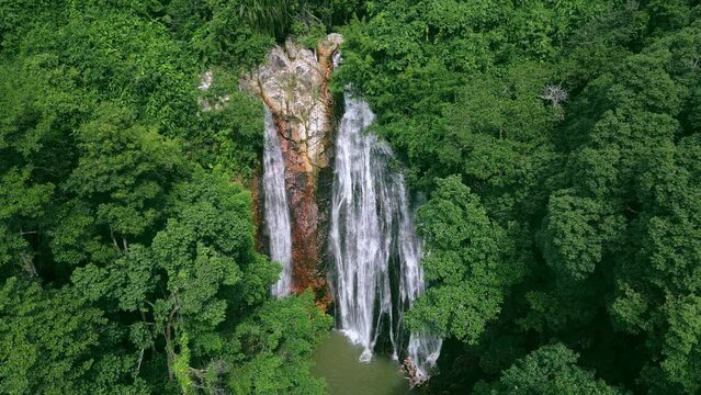 Beautiful waterfall in tropical forest surrounded by dense green vegetation. Jets waterfall noisily fall down between rocks leaving tiny splashes. In vicinity of waterfall area looks truly heavenly.