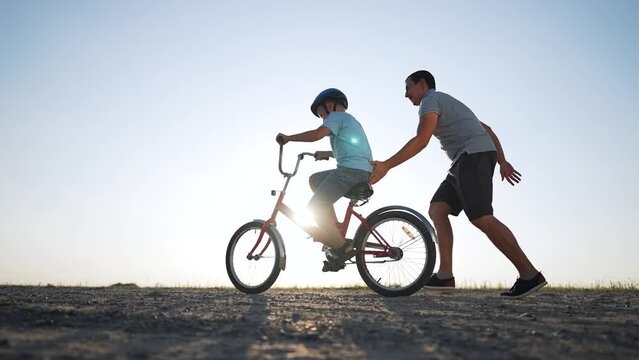 Father's Day. Father teaches son to ride bicycle wearing safety helmet. child learn to ride bicycle in park at sunset. Happy family concept and dream. Active father teaches child to ride bike in park