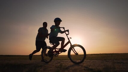 Happy family.Father teaches son to ride bike in park. son riding bike for first time.Kid dream of traveling by bike. Kid is learning to ride bike.Father helping hand to son.Active happy family in park