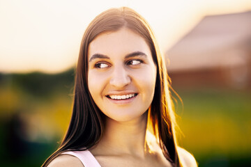 Portrait of Caucasian brunette female in her 20s , in light of setting sun against blurred background of rural landscape, close-up.