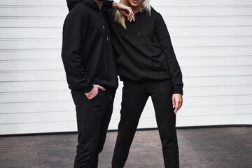 A trendy couple poses outdoors in black hoodies for a mock-up design. A fashion template for print...