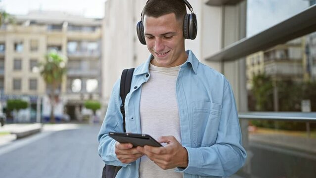 Smiling hispanic man with headphones using tablet on urban street