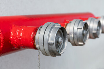 Red fire hose and water tap on white wall background