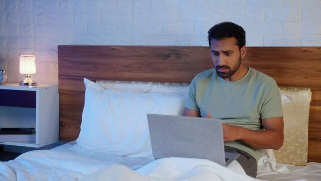 Indian businessman working on bed at midnight with clients meeting - concept of deadline, corporate lifestyle and project negotiation.