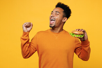 Young fun overjoyed man he wear orange sweatshirt casual clothes eat classic burger do winner...