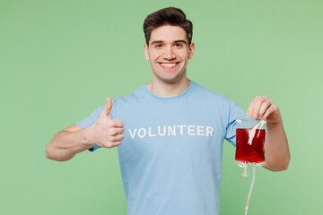 Young happy donor man wears blue t-shirt white title volunteer hold bag with blood show thumb up...