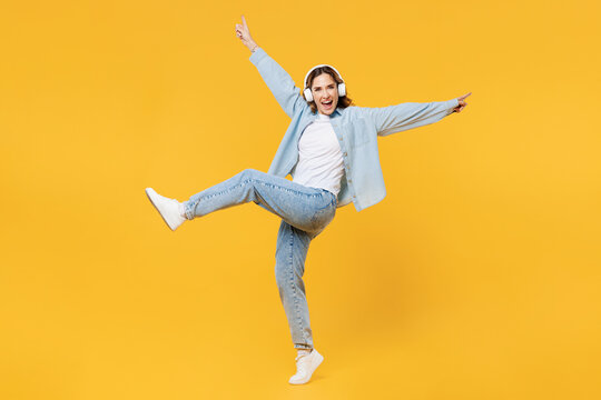 Full Body Young Woman Wear Blue Shirt White T-shirt Casual Clothes Use Mobile Cell Phone Listen To Music On Headphones With Outstretched Hands Isolated On Plain Yellow Background. Lifestyle Concept.