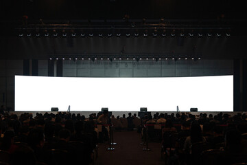 Front view of mockup on big blank white screen with space in empty huge hall with scene and silhouette of audiences