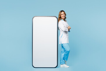 Full body side view doctor woman she wear white medical gown suit work in hospital clinic office big huge blank screen mobile cell phone isolated on plain blue background Health care medicine concept