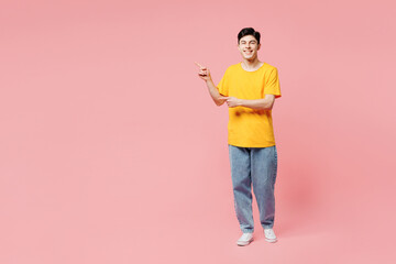 Full body smiling cheerful young man he wears yellow t-shirt casual clothes point index finger aside on area mock up isolated on plain pastel light pink background studio portrait. Lifestyle concept.