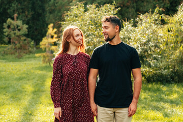 Fototapeta premium Outdoors shot of happy couple standing straight in park looking at each other on a sunny day.