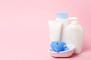 Baby bath accessories. Child care. Miniature toy in small bathtub with shampoo, cream and lotion bottles on pink background with copy space