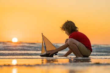 Kid playing on the beach. Child play on the sea with toy ship boat. Little child having a happy...