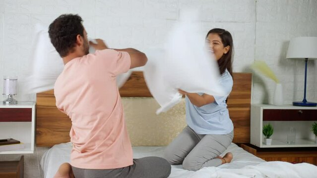 Playful indian couples fighting with pillows at bedroom - concept of intimacy, flirting and joyful relationship bonding