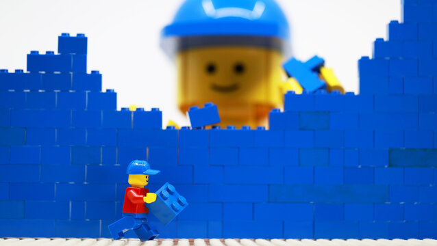 Hong Kong -February 15 2024: giant man build a brick wall piece by piece with his little helper 