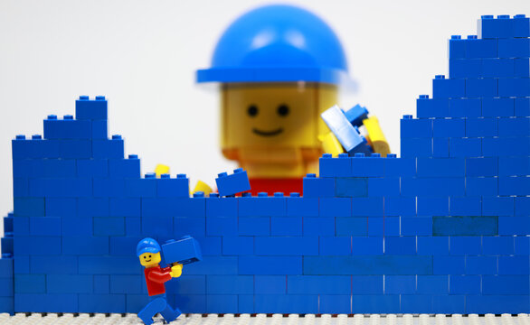 Hong Kong -February 15 2024: giant man build a brick wall piece by piece with his little helper 