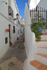 A picturesque narrow and steep cobbled alley in Frigiliana, Axarquia, Malaga province, Andalusia, Spain, with traditional whitewashed little houses and decorated with colorful flowers and plants