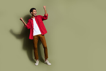 Full length photo of lucky cheerful guy wear red shirt yelling yeah rising fists empty space...