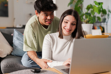 Cheerful young couple sitting on a sofa together, using a laptop in a relaxed home environment