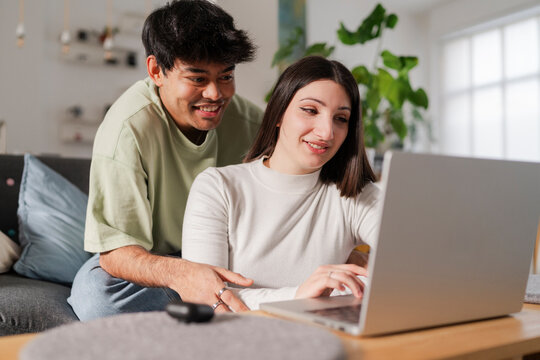 Cheerful young couple sitting on a sofa together, using a laptop in a relaxed home environment