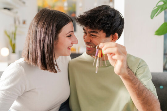 Smiling young couple excitedly holding a bunch of colorful keys, celebrating a new home ownership together