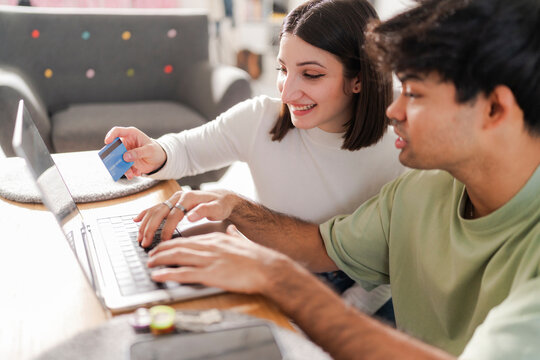 Happy couple engaged in an online purchase, with the man holding a credit card and the woman typing on a laptop