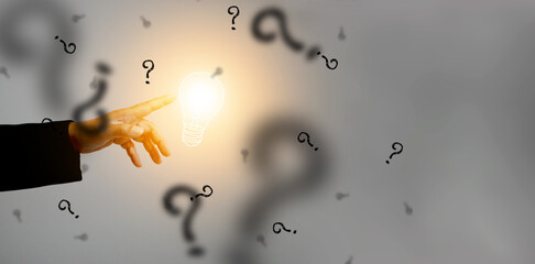 Idea concept. Hand touches an illuminated light bulb surrounding by black question marks. Lightblub...
